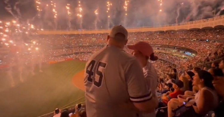 Man stands next to his girlfriend, an arm around her, as they watch fireworks at a Yankees game.