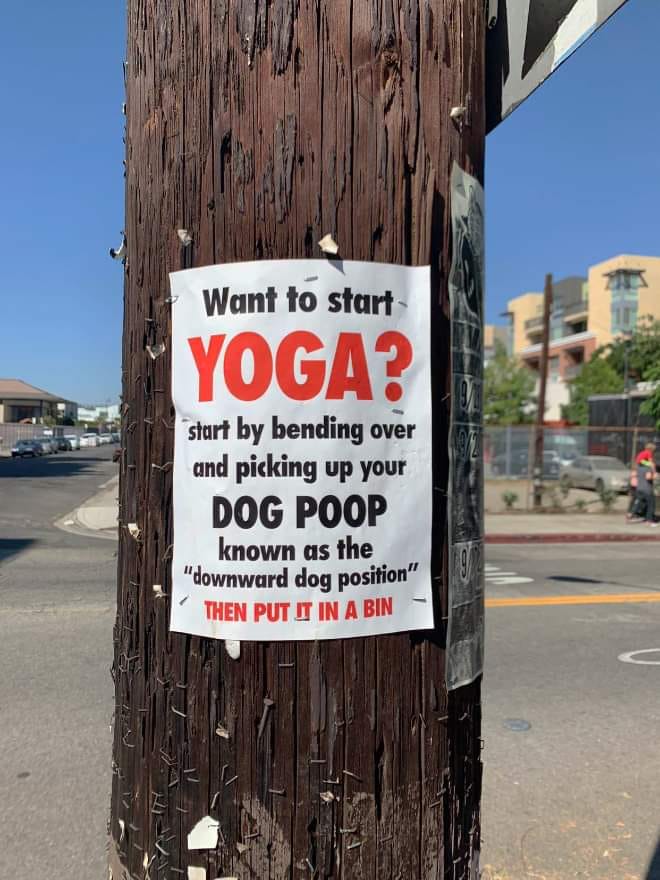 Sign on a wooden pole near a street. It reads "Want to start yoga? Start by bending over and picking up your dog poop known as the "downward dog position" then put it in the bin."
