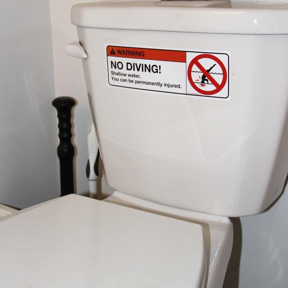 Sign on a toilet that reads "Warning. No diving! Shallow water. You can be permanently injured" along with an image of a stick figure person diving into water with a red x over it.