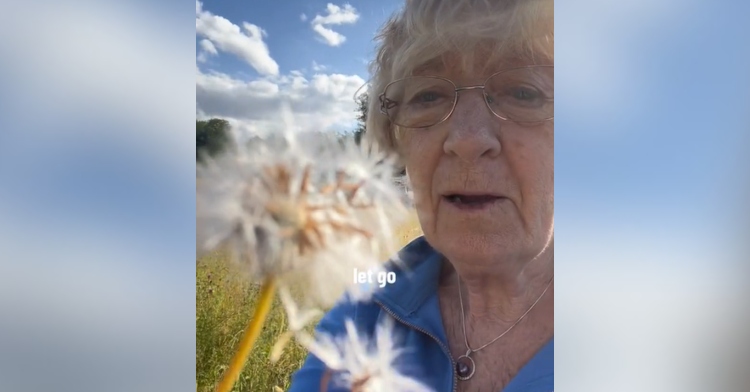 82-year-old grandma sits in a field holding a dandelion. Words on the image show what she's saying: "Let go."