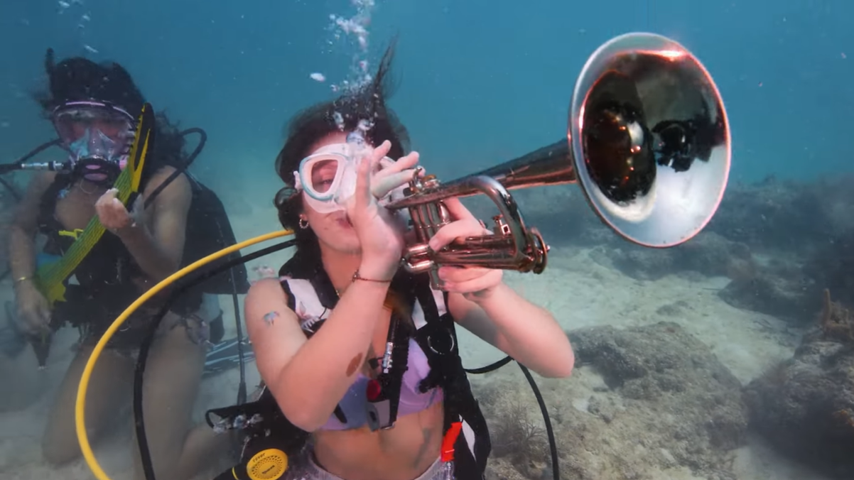 Two divers dressed as mermaids pretend to play instruments together. One has a trumpet and the other has some type of guitar. They are a part of the 39th annual Lower Keys Underwater Music Festival at Looe Key Reef.