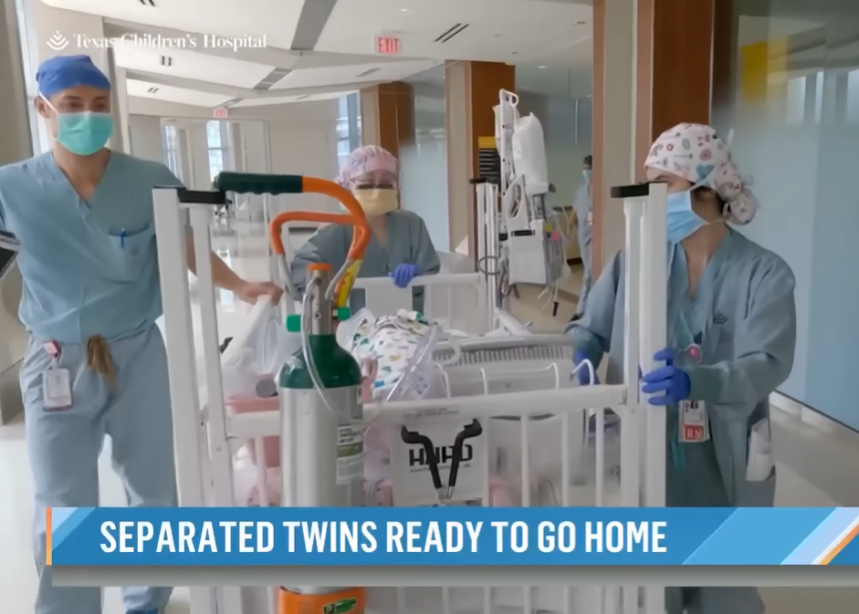 Doctors roll the Fuller twins in a hospital bassinet down a hall. 