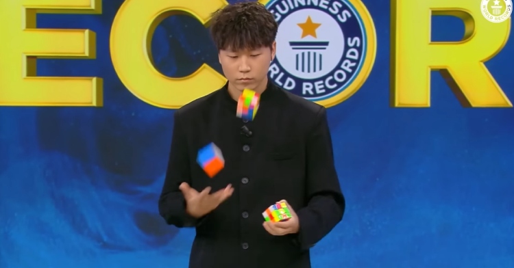 22 year old man concentrates as he juggles and solves three Rubik's cubes.