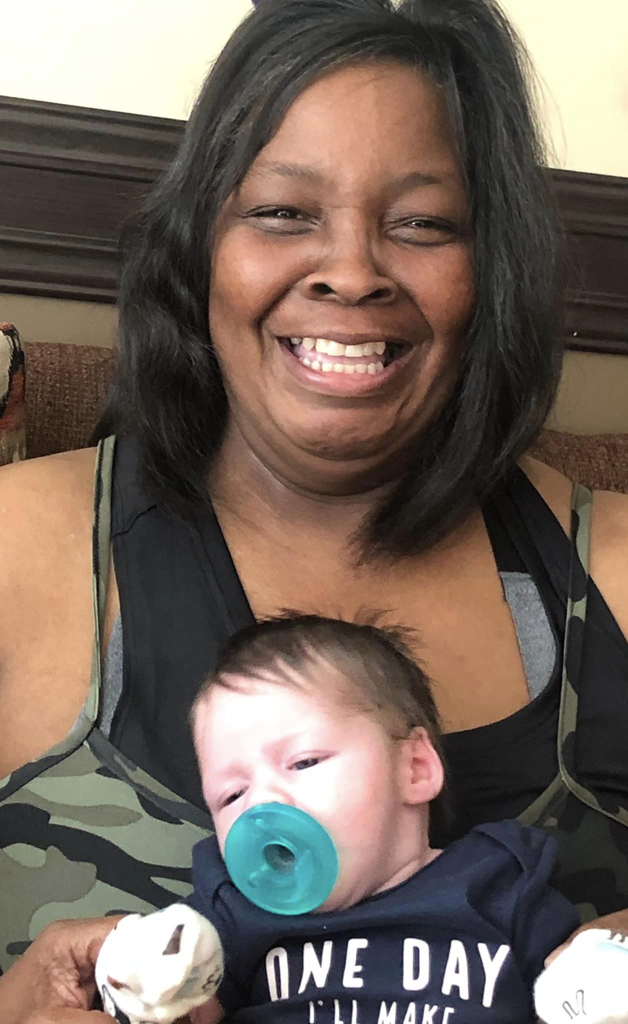 A woman smiles wide as she sits and holds a baby in her arms.