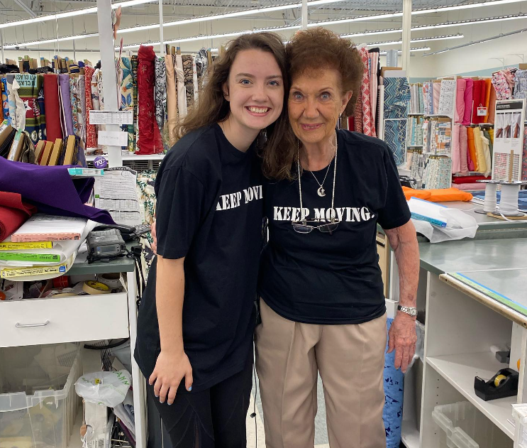 Maggie HusVar and Jayne Burns smile as they pose for a photo in the fabric department of Joann. They're wearing matching shirts that say "Keep Moving."