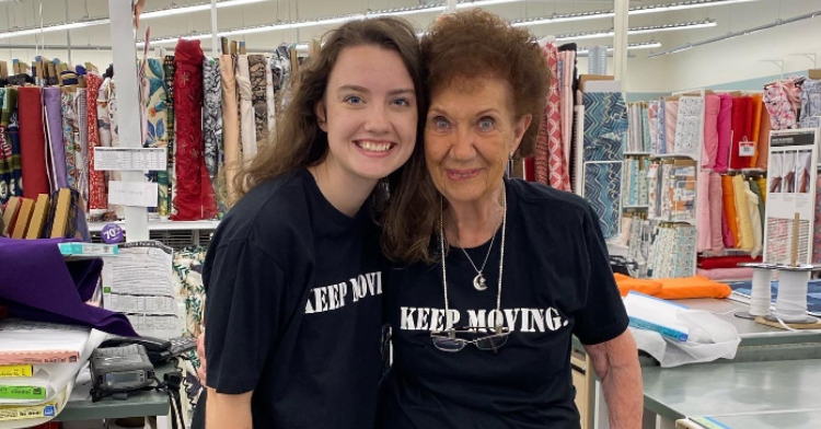 Maggie HusVar and Jayne Burns smile as they pose for a photo in the fabric department of Joann. They're wearing matching shirts that say "Keep Moving."