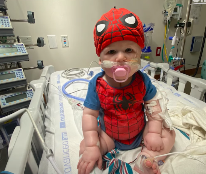 baby wearing Spider-Man gear in a hospital bed.