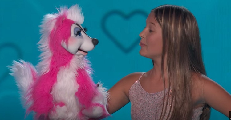 A young ventriloquist speaking with a pink skunk.