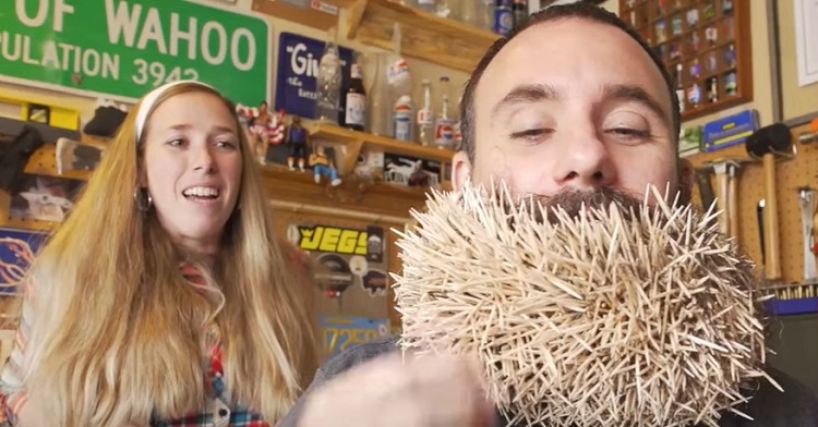 Image shows a wife looking on apprehensively as husband pushes toothpicks into his beard to break a world record