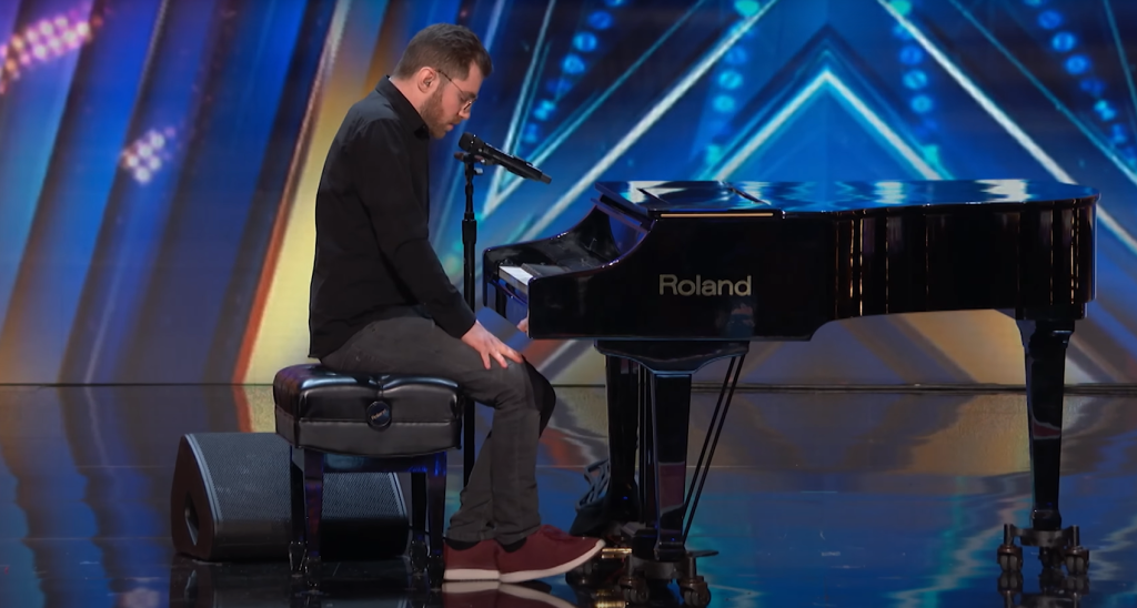 Man sits at piano, nervously looking down, just before a surprise reveal.