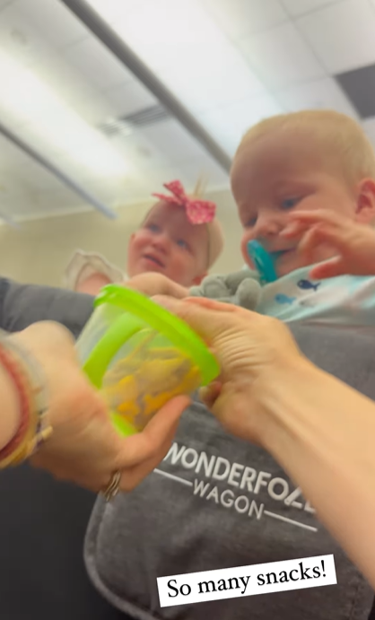 View from Torrey's perspective of her feeding two of her triplets from a small food container. One baby happily grabs at the food while the other looks into the distance. Words on the image read "So many snacks!"