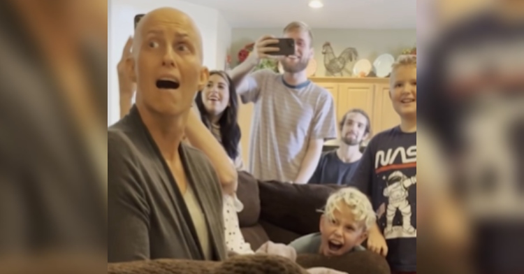A bald woman looks shocked with her mouth open and her eyes wide. She and five other look at something that can’t be seen in the photo. Everyone looks elated.