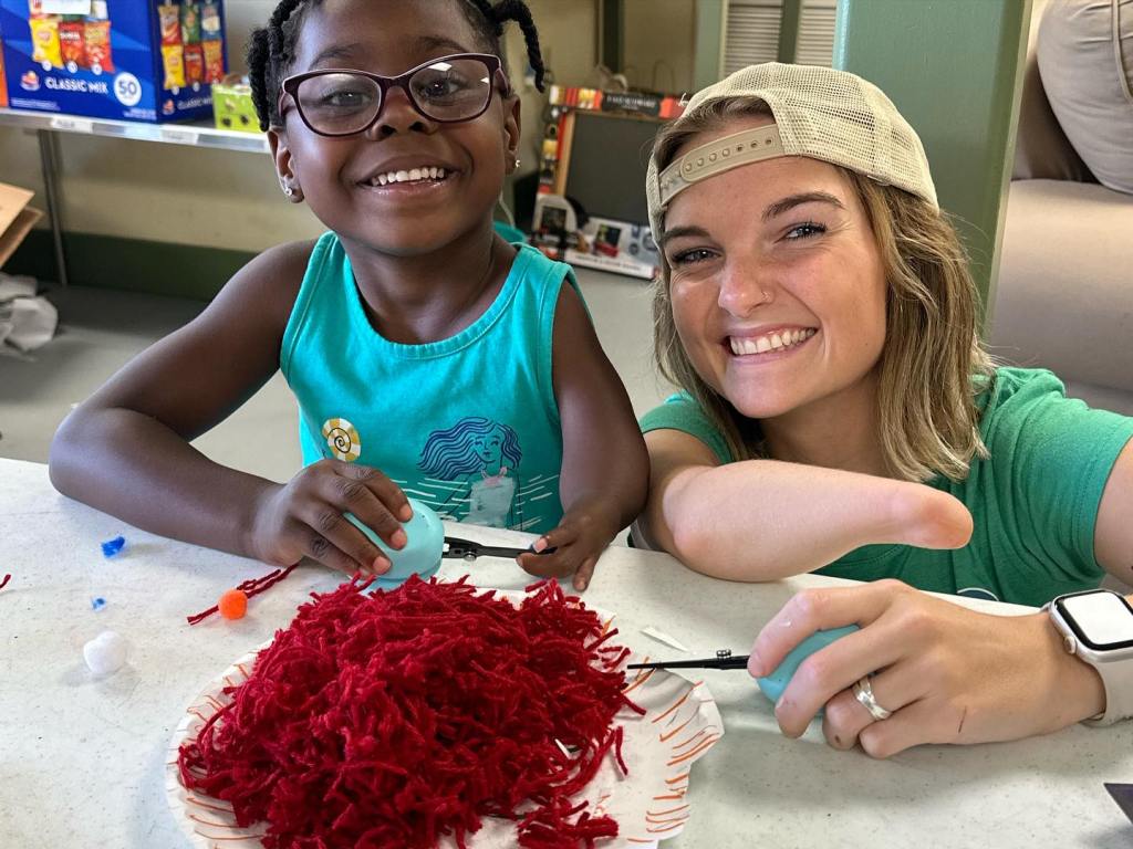 a woman with a limb difference sitting next to a kid with glasses in front of a plate full of yarn