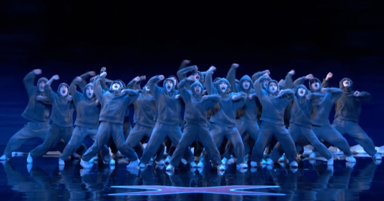A large group of people lit up in blue dance in unison in an otherwise pitch black stage on "America's Got Talent."