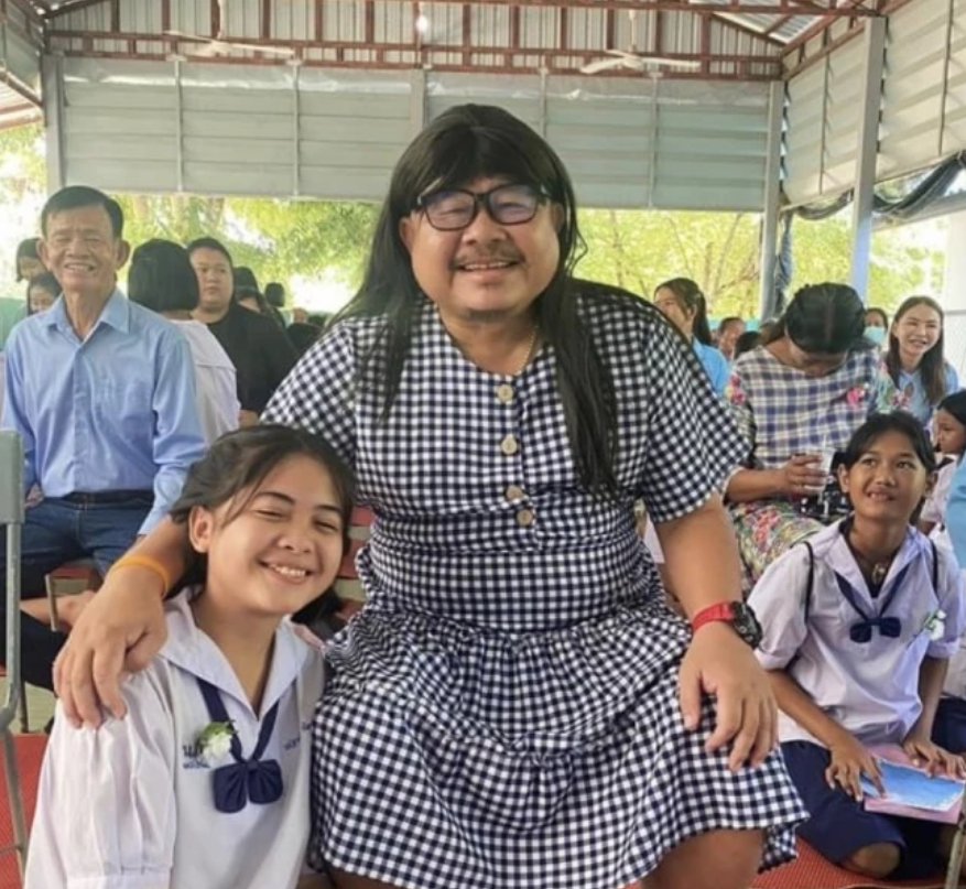 Child pictured with father wearing checkered dress and wig for Mother's Day.