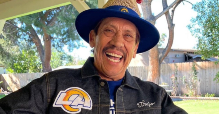 Close up of actor Danny Trejo smiling wide while standing outside.