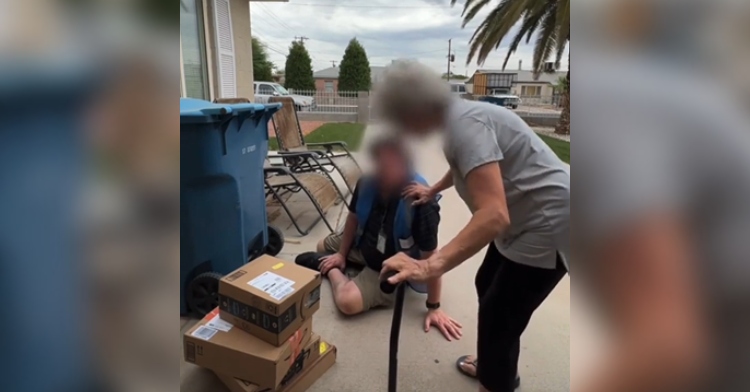A woman with a cane places a hand on the shoulder of a delivery driver who is sitting in the driveway of her home. Both of their faces have been blurred out to conceal their identities.