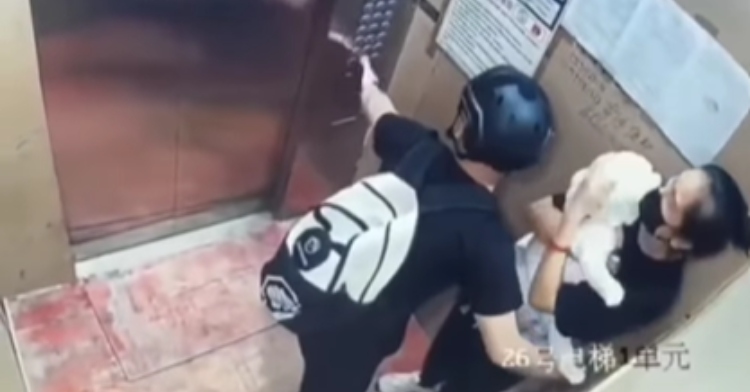 On an elevator, a man protects a woman and her baby while pressing buttons to help free them.