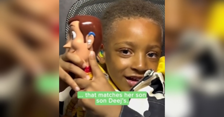 5-year-old smiles as he holds up a Woody doll wearing a hearing aid that matches his own.