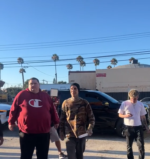 Travis Barker stepping out of car holding 2 sets of drumsticks.