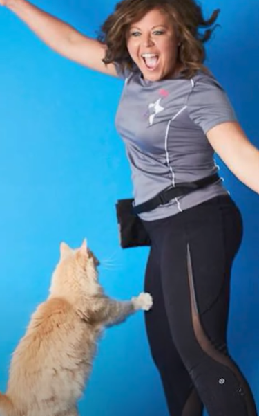 Trisha smiles as she leaps into the air with Kit Kat the cat leaping with her, his paws reaching out.