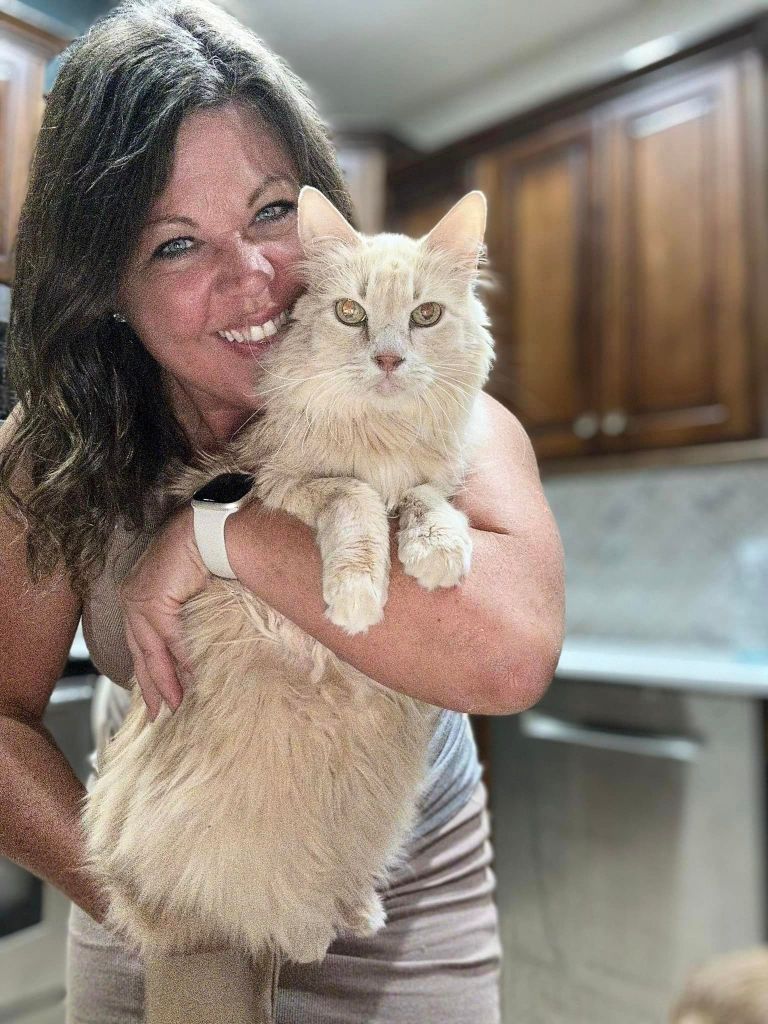 Trisha smiles wide as she holds Kit Kat for a photo. The cat is staring directly into the camera.