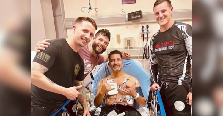 Plymouth police Stgt. Donny Reddington, Det. David Ross, and firefighter Nick Robbins smile as they stand next to George who is sitting in a hospital bed. George smiles and gives two thumbs up despite being hooked up to several machines.