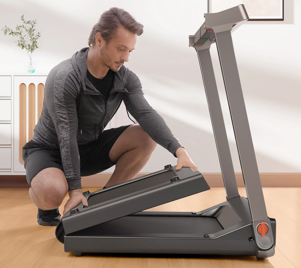A man is kneeling as he folds up the Kingsmith Walking Pad Double Fold G1SE Treadmill.