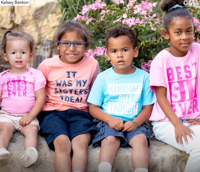 John and Amy's four children sit outside on a rock pillar in front of flowers. This includes Ora who, at this point, is old enough to walk.