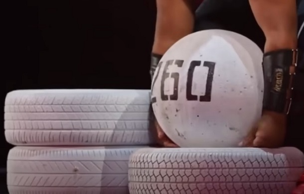 A contestant on the AGT stage lifts a 260 pound stone. The image shows the stone and two platforms made using automotive tires painted white.