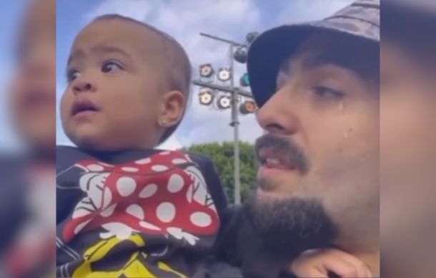 Image shows a father holding his daughter up at a parade. He is crying at her reaction to the sights and sounds.