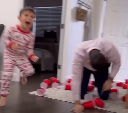 Dad performing a fake fall and pretending to be surprised as his three boys play a prank on him.