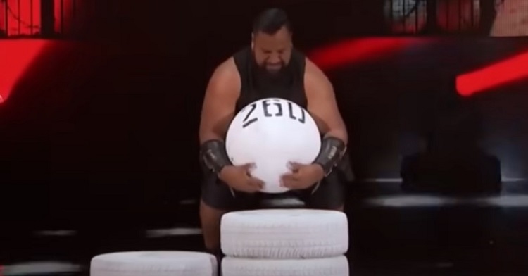 A strongman entertains the AGT audience by lifting a 260 pound round stone on the stage.