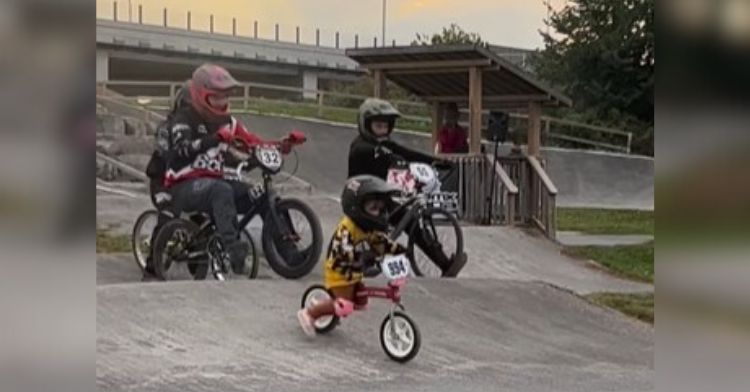 Image shows a BMX Race with a tiny tot leading a group of teenaged riders.