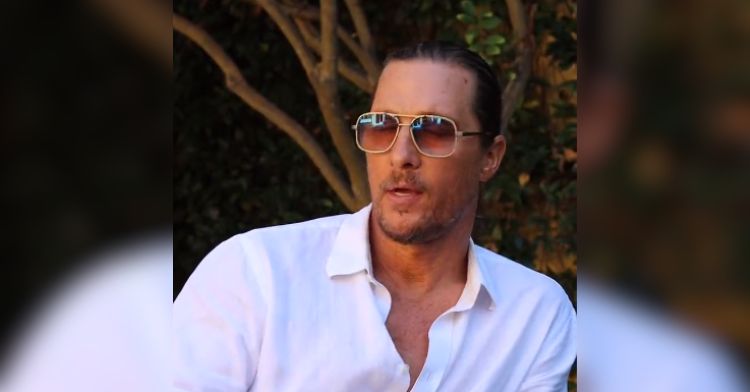 Matthew McConaughey on the pursuit of happiness. Image shows the star seated, in a white shite with several buttons undone, wearing lightly shaded glasses.