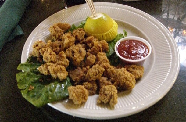 Image shows one of the regional foods available in the US. An order of Rocky Mountain Oysters with red cocktail sauce in a small bowl on the plate.