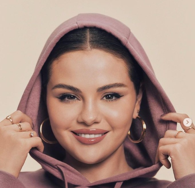 Inspiring a new generation, Selena Gomez appears in this image wearing a hoodie, large hoop earrings, and several rings.