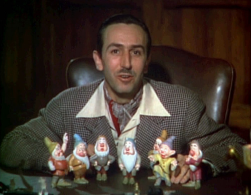 Walt Disney spent his lifetime inspiring and entertaining audiences. This image shows him seated at a desk with figurines of the seven dwarves in front of him.