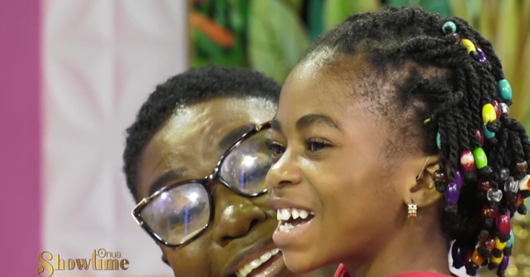 Abigail Adjiri smiles wide, hearing aid in her ears, as she counts to 10 with the "Onua Showtime with Nana Ama McBrown" audience. Abigail is sitting on someone's lap.