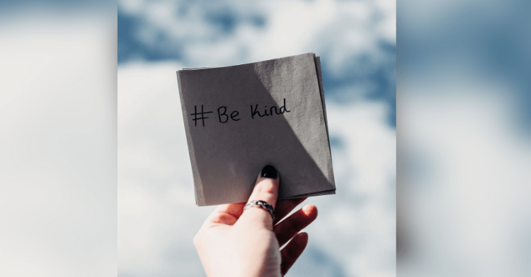 hand holding out a post it saying "be kind"