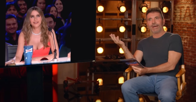 Simon Cowell talks as he sits next to a TV that's displaying a picture of Sofia Vergara where she's rolling her eyes at Cowell.