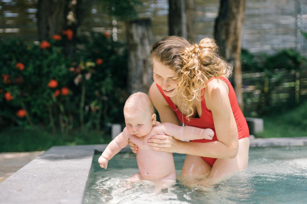 a woman holding a baby while in the swimming pool