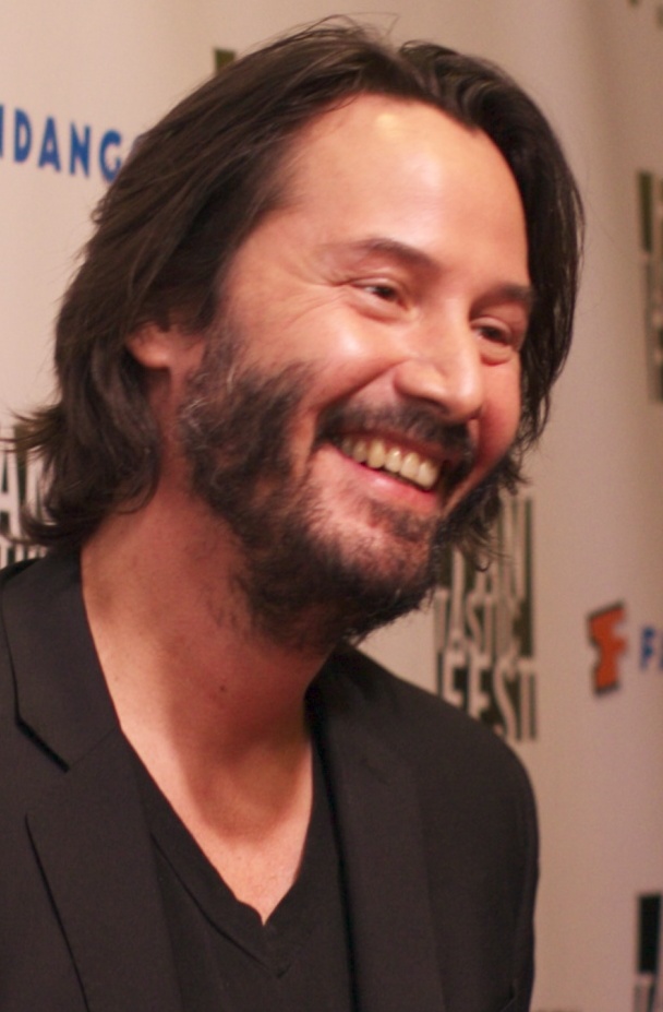 Close up of Keanu Reeves smiling wide.