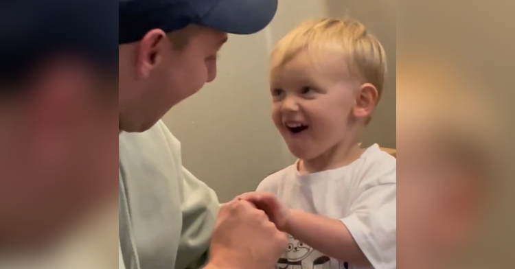 Little boy smiles wide as he holds dad's hand.