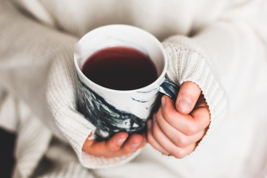 Top-down view of someone holding a mug of tea. Their sweater is so long it covers much of their hands.