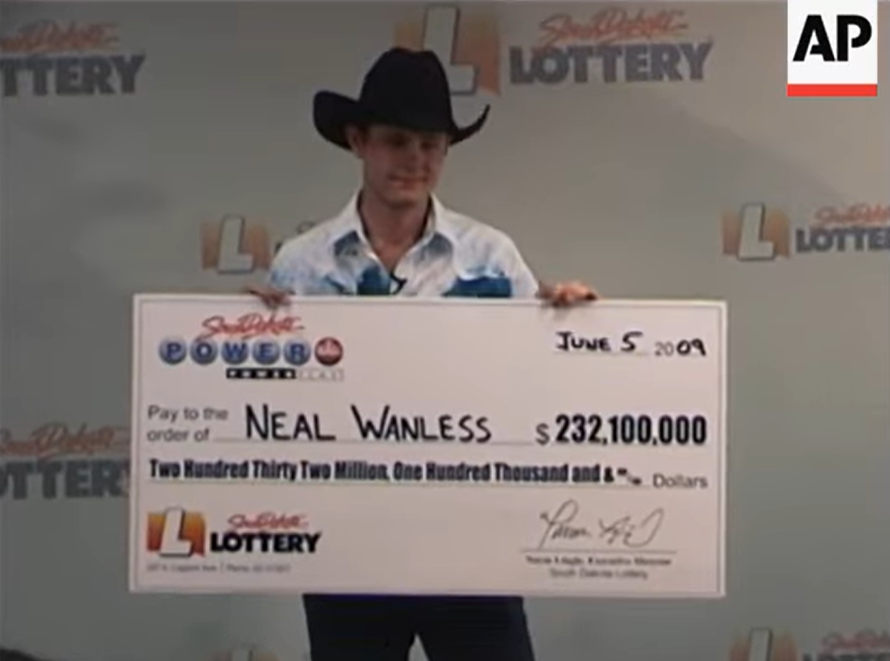 Neal Wanless smiles as he wears a cowboy hat and poses for photos with a giant check showing he won the lottery.