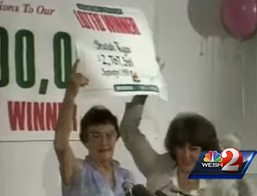 With the help of another woman, Sheelah Ryand lifts a giant sign into the air showing that she won the lottery.