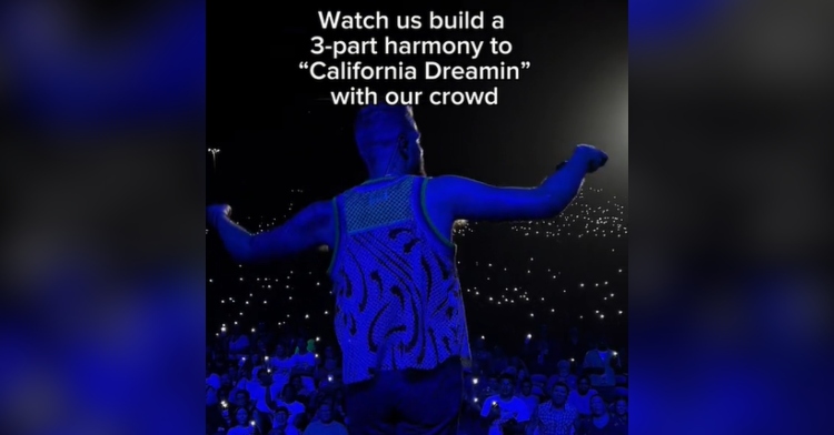 Scott Hoying of Pentatonix leads a crowd in Dallas at a concert to sing. The lights on the stage make the space look blue. Text on the image reads: Watch us build a 3-part harmony to “California Dreamin” with our crowd