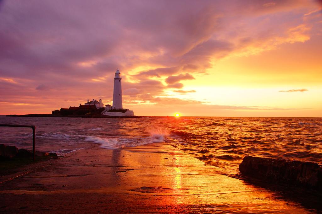 A beautiful sunset over the ocean with a lighthouse in the distance.