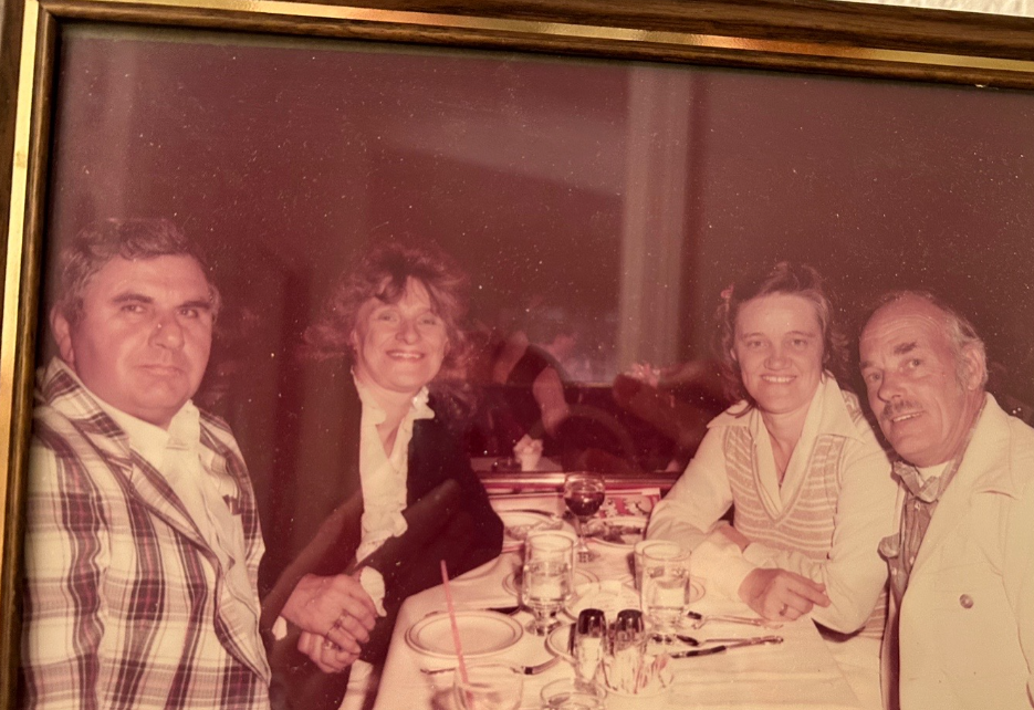 Framed photo of a young Barbara Carolan and Shirley sitting at a restaurant table with two men. Everyone is smiling.